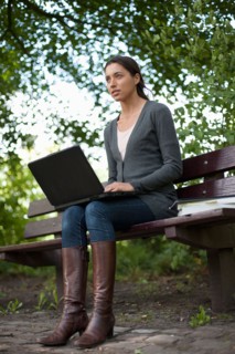 Young woman sitting on park bench using laptop. Photo : Jan Scherders