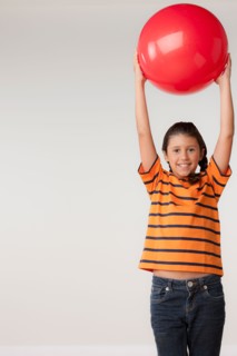 Studio portrait of girl (8-9) holding red ball. Photo : Rob Lewine