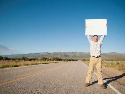 Mid-adult man hitch-hiking in barren scenery.