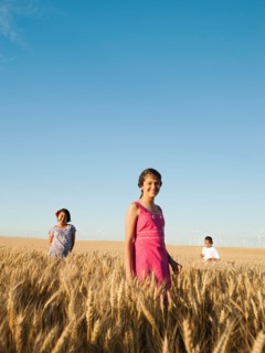 Girls (10-11, 12-13) and boy (8-9) standing in wheat field.