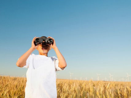 Boy (8-9) standing in wheat field, looking through binoculars.