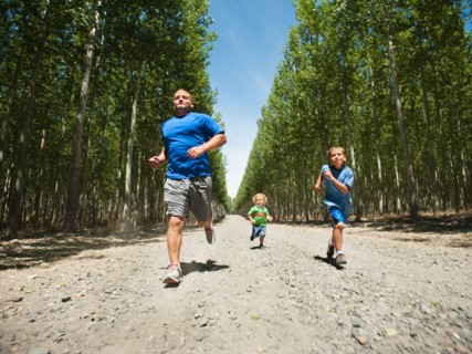 Father with sons (2-9) running down country road.
