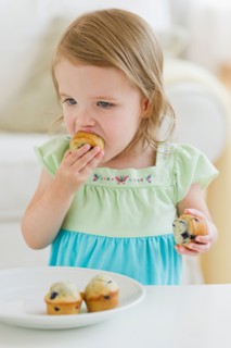 Girl (2-3) eating muffins.