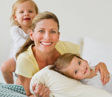 Portrait of mother with daughters (2-3) on bed.