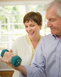 Senior man lifting dumbbell, nurse assisting him.