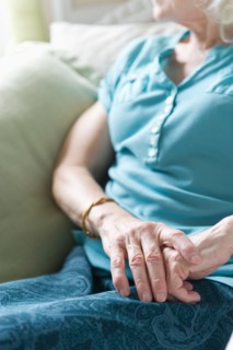Senior woman sitting in chair, close-up of hands.