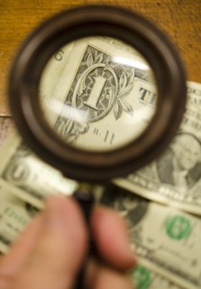 Hand holding magnifying glass over dollar bills, studio shot.