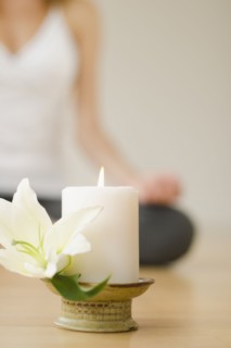 Candle and flower with woman practicing yoga in background, studio shot.