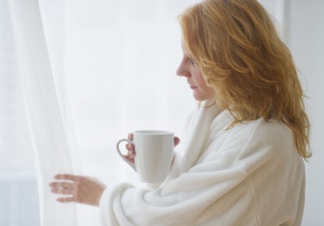 Woman in bathrobe looking out window.