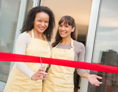 Two female business owners cutting red ribbon.