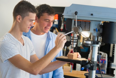 Man with teenage son (16-17) drilling in workshop.