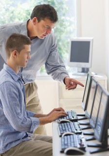 Teacher helping teenage student (16-17) in computer lab.