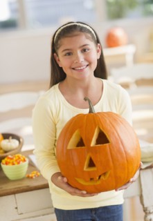 Portrait of girl (10-11) holding Jack o lantern.