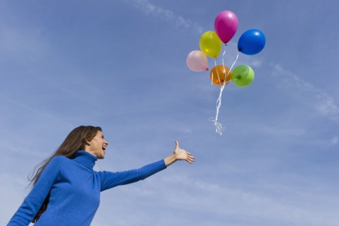Smiling woman loosing balloons.