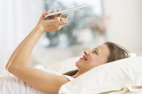 Woman using digital tablet in bed.