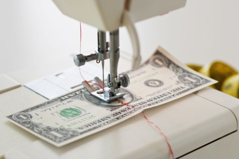 Halves of dollar bill being sewed with sewing machine.
