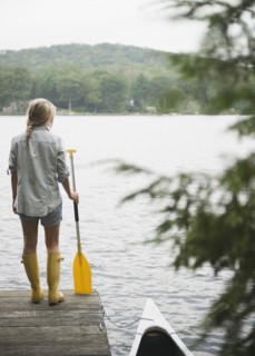 USA, New York, Putnam Valley, Roaring Brook Lake, Woman standing on pier with paddle. Photo: Jamie