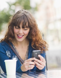 Woman sitting in sidewalk cafe and texting on mobile phone. Photo : Daniel Grill