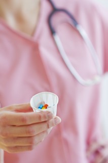 Close up of hand of female nurse holding cup with pills. Photo: Daniel Grill