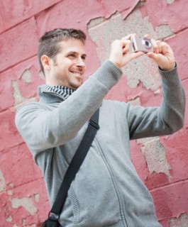 Man standing at front of old peeling red wall and photographing. Photo : Daniel Grill