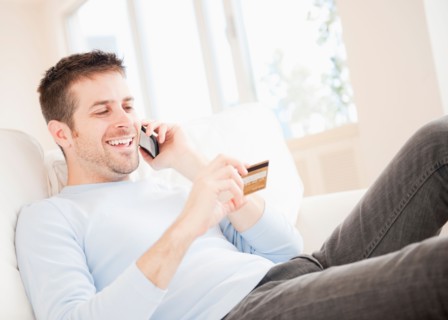 Man talking on mobile and holding credit card. Photo : Daniel Grill