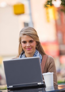 Young woman sitting with laptop in sidewalk cafe. Photo : Daniel Grill
