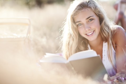 Teenage girl (16-17) posing for portrait while reading book outdoors. Photo : Take A Pix Media
