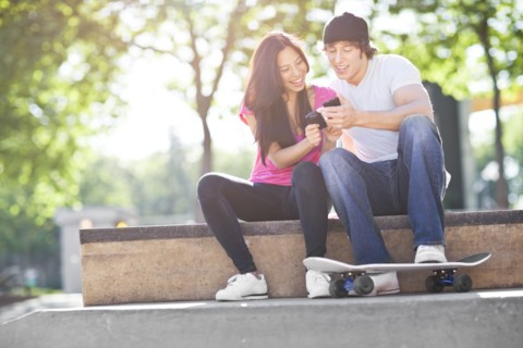Young multi-racial couple sitting with skateboard, using mobile phone. Photo : Take A Pix Media