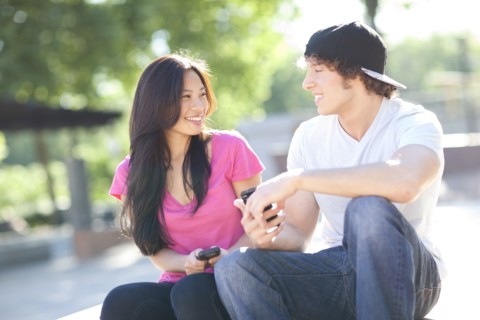 Young multi-racial couple sitting together playing with their mobile phones. Photo : Take A Pix