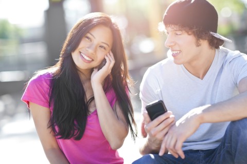 Young multi-racial couple sitting together playing with their mobile phones. Photo : Take A Pix