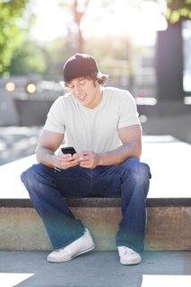Young man sitting outdoors, text messaging. Photo : Take A Pix Media