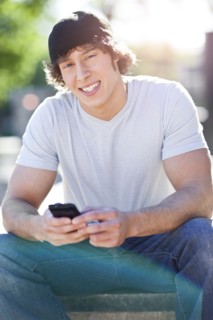 Young man sitting outdoors, text messaging. Photo : Take A Pix Media