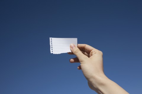 Hand of woman holding paper note against blue sky. Photo : Winslow Productions