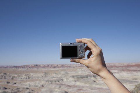 Hand of woman holding camera up against blue sky. Photo: Winslow Productions