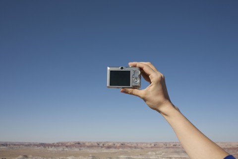 Hand of woman holding camera up against blue sky. Photo: Winslow Productions