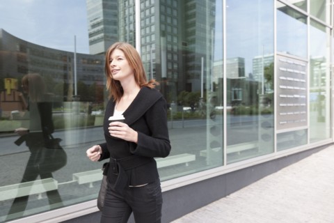 The Netherlands, Amsterdam, Businesswoman walking with coffee. Photo : Jan Scherders