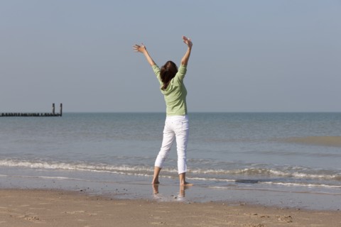 Woman on beach with arms raised. Photo : Jan Scherders