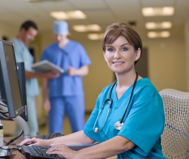 Female surgeon working on computer in hospital, colleagues in background. Photo : db2stock