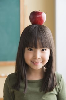 Portrait of girl (6-7) balancing apple on head. Photo : Rob Lewine