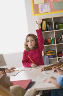 Girl (6-7) rising her hand in classroom. Photo : Rob Lewine
