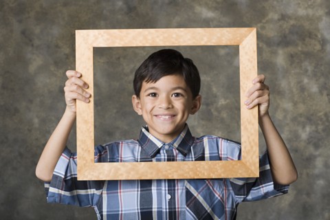 Portrait of smiling boy (8-9) looking through frame, studio shot. Photo: Rob Lewine