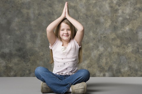 Smiling girl (8-9) sitting cross-legged with hand over her head, studio shot. Photo : Rob Lewine