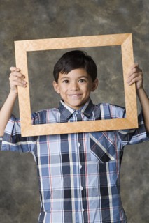 Portrait of smiling boy (8-9) looking through frame, studio shot. Photo: Rob Lewine