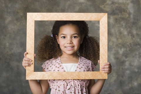 Portrait of smiling girl (8-9) holding picture frame, studio shot. Photo: Rob Lewine