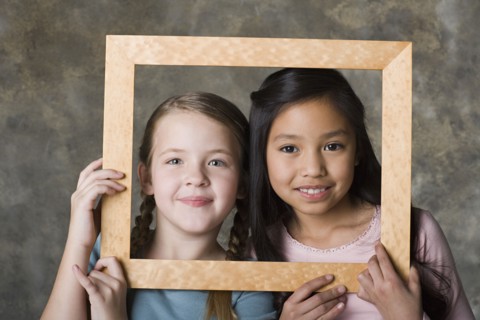 Portrait of girls (8-9) looking through picture frame, studio shot. Photo: Rob Lewine