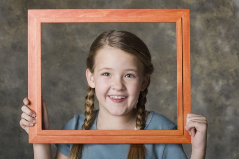 Portrait of smiling girl (8-9) holding frame, studio shot. Photo: Rob Lewine