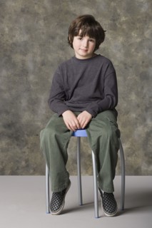 Smiling boy (6-7) sitting on chair, studio shot. Photo : Rob Lewine