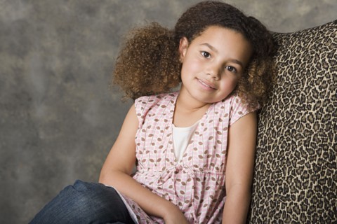 Portrait of smiling girl (8-9) sitting on chair, studio shot. Photo : Rob Lewine