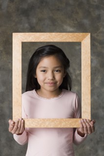 Portrait of smiling girl (8-9) holding picture frame, studio shot. Photo: Rob Lewine