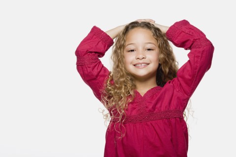 Portrait of smiling girl (8-9) with hands on head, studio shot. Photo: Rob Lewine